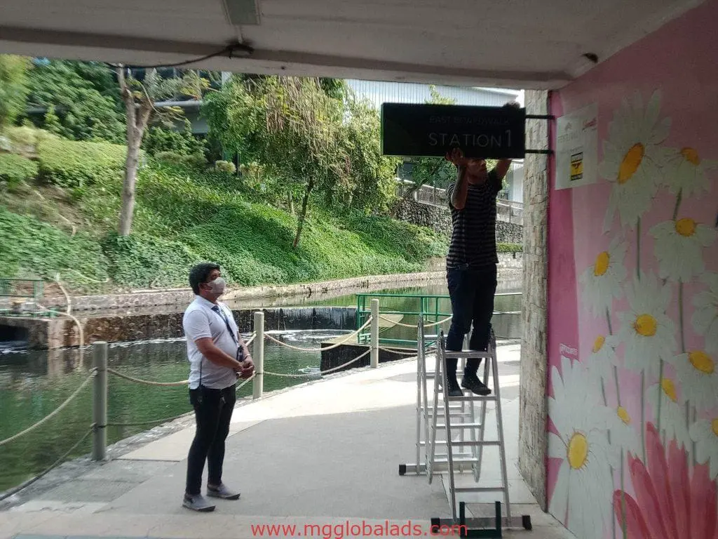 Outdoor acrylic signage installation for Station 1 client, Makati, with floral mural and workers adjusting sign by M&G Global Ads.
