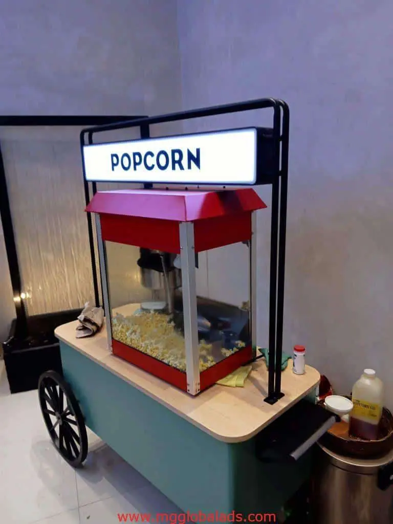 Metallic POPCORN signage above popcorn cart and machine, bottles arranged neatly, indoor Makati event by M&G Global Ads.