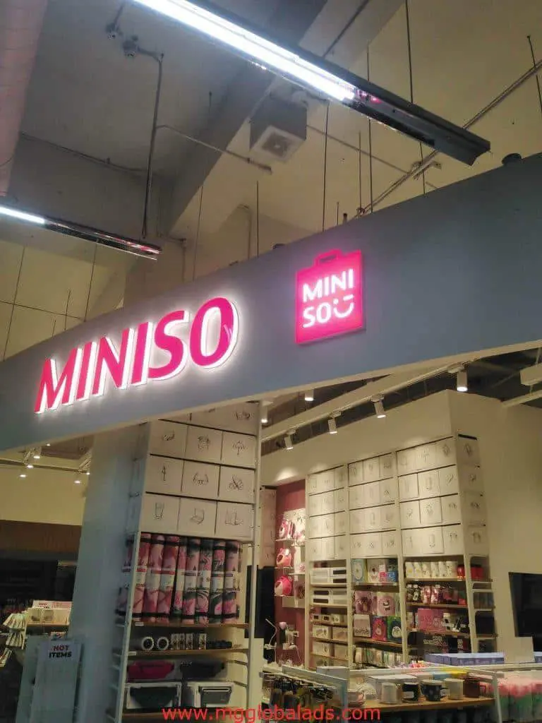 MINISO lighted pink and white building signage at Quezon City storefront; organized household displays inside by M&G Global Ads.