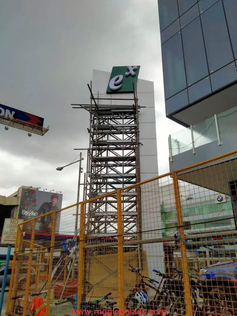Acrylic signage for ex logo client at construction site in Mandaluyong, with scaffolding and bikes, by M&G Global Ads.