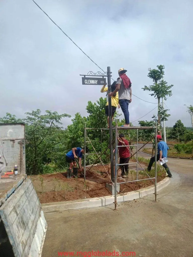 Metal pylon signage installation for GLENWAY by four men in Quezon City, surrounded by trees and greenery, by M&G Global Ads.