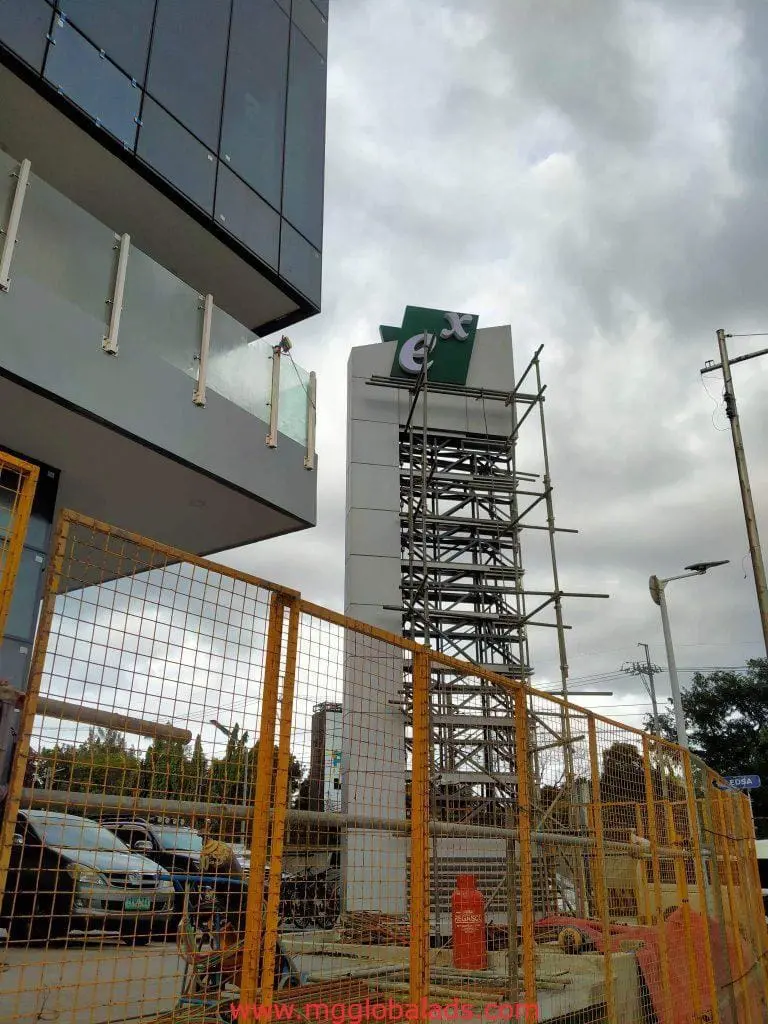 Billboard signage installation with scaffolding in Makati, orange barriers, cars, and building under clouds by M&G Global Ads.
