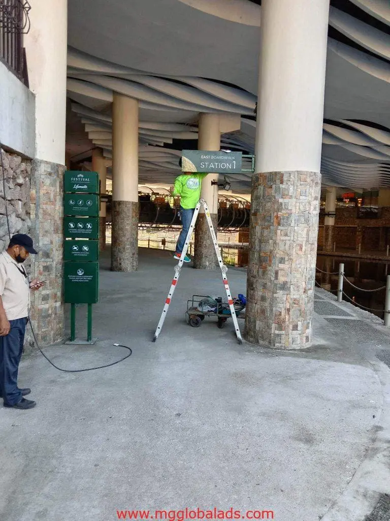 Outdoor sign installation for Station 1 East Boarding in Makati, a worker on ladder, cable held nearby, by M&G Global Ads.