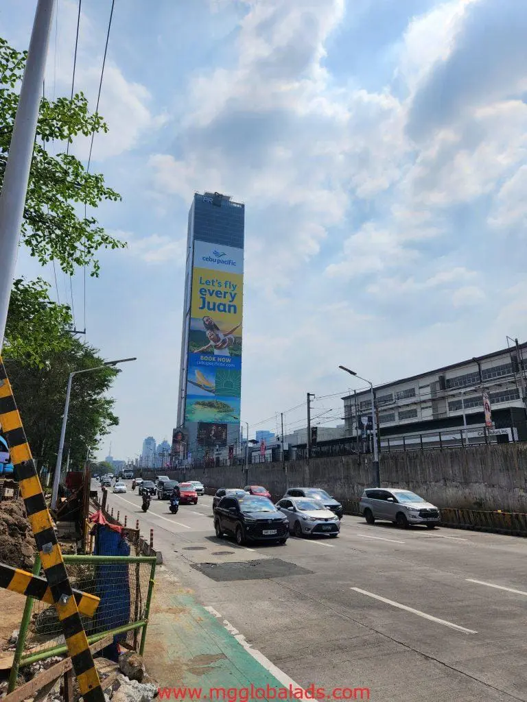 LED signage for Cebu Pacific at a Makati skyscraper, cars below, trees and barriers on left sidewalk by M&G Global Ads.