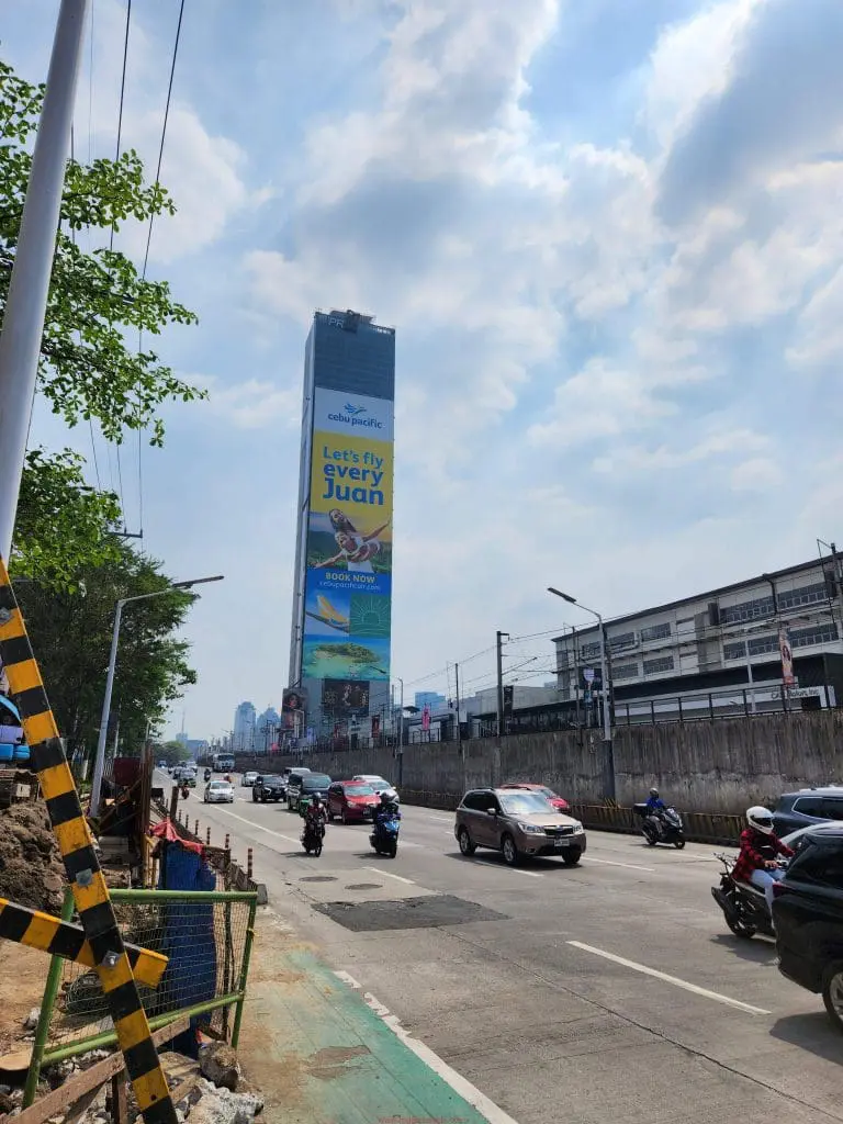 Cebu Pacific outdoor billboard signage on a tall building in Makati, busy street view, cars passing by. by M&G Global Ads.