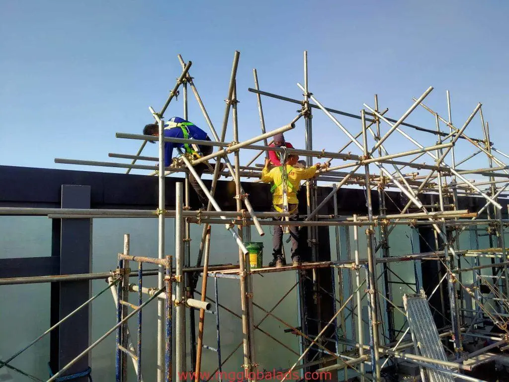 Construction workers installing building lighted signage on scaffolding in Quezon City under clear sky by M&G Global Ads.