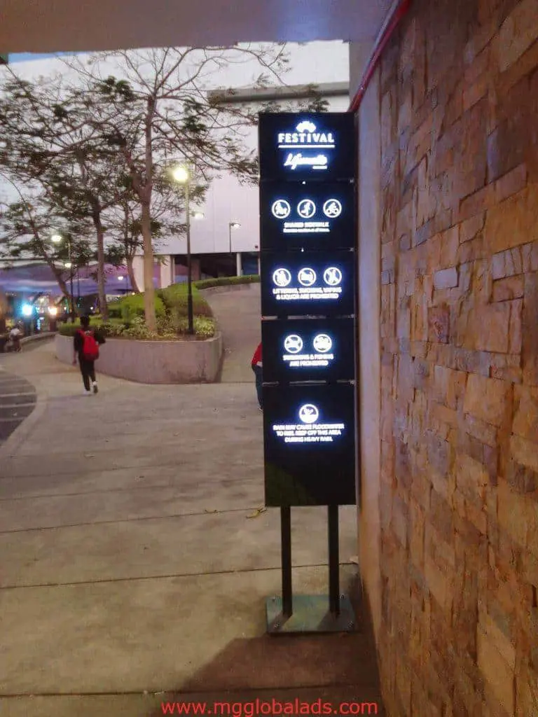 Acrylic mall entrance signage with glowing rules icons in Makati, stone wall and pathway beside it by M&G Global Ads.