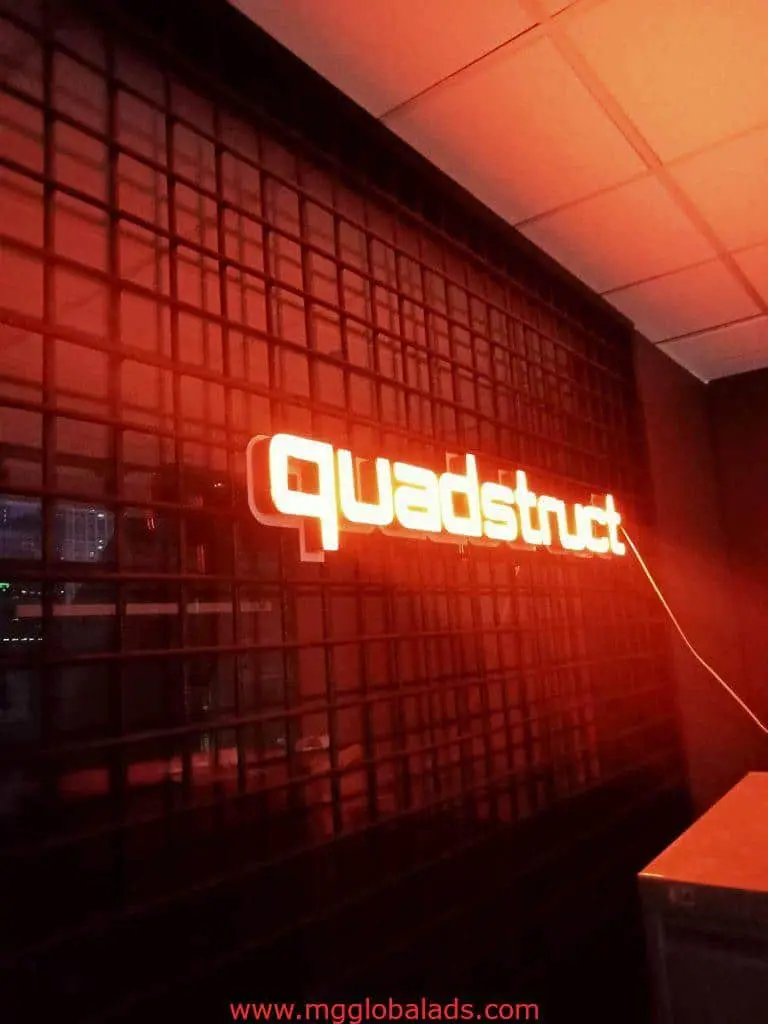 Orange neon acrylic signage for quadstruct on black grid wall in Makati office, white tiled ceiling. By M&G Global Ads.