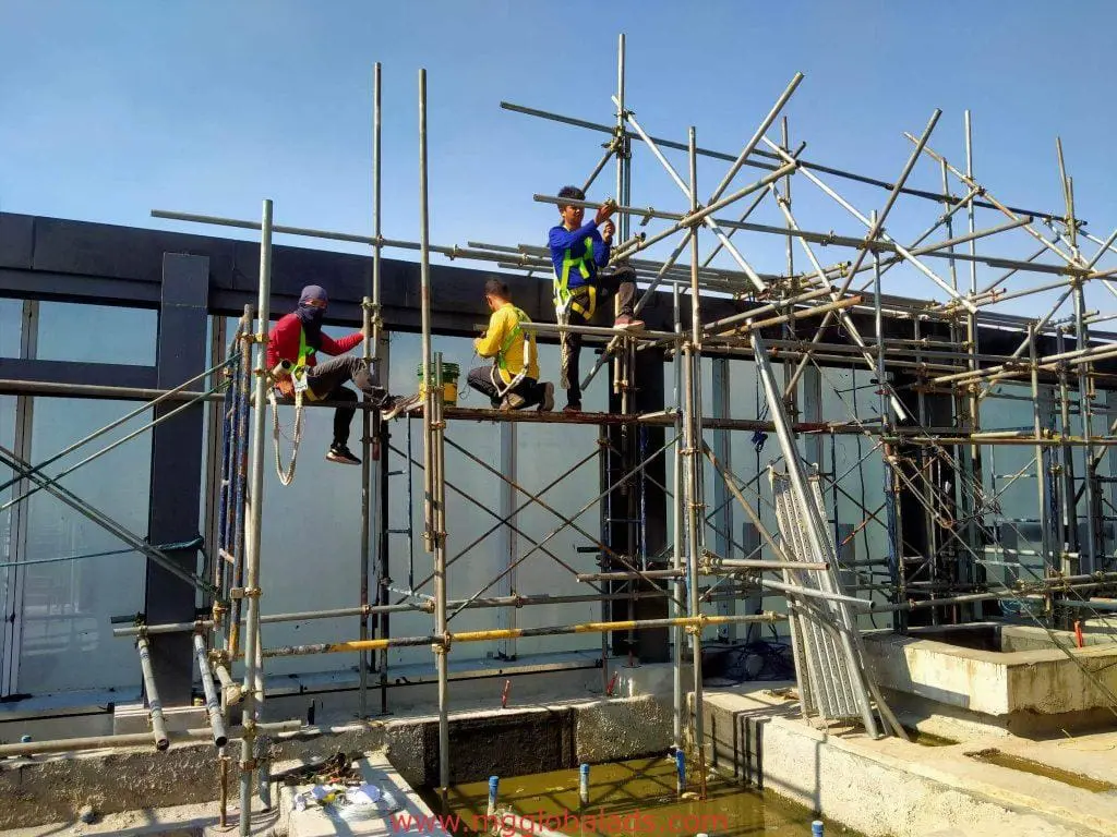 Construction workers on scaffolding install outdoor building signage in front of a glass facade in Makati by M&G Global Ads.