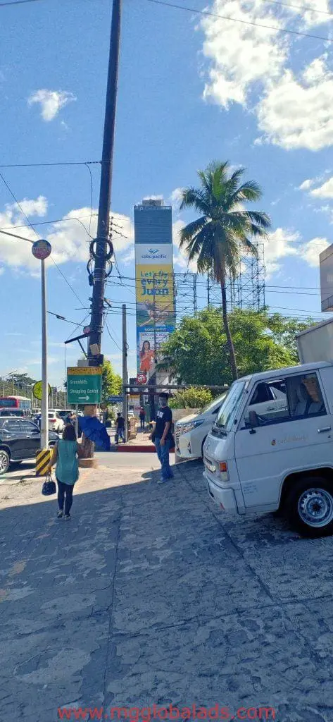 LED billboard advertising in Makati on a tall building above busy street with pedestrians, van, palm tree by M&G Global Ads.
