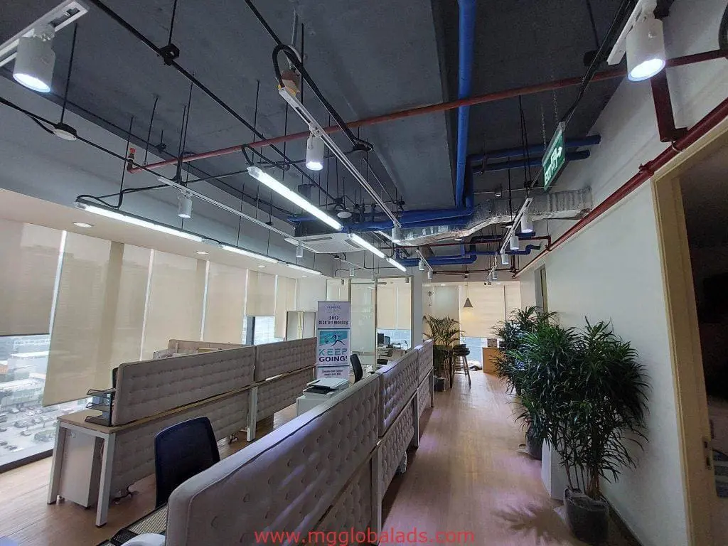 Metallic office signage in Makati workspace with white desks, indoor plants, and exposed pipes by M&G Global Ads.