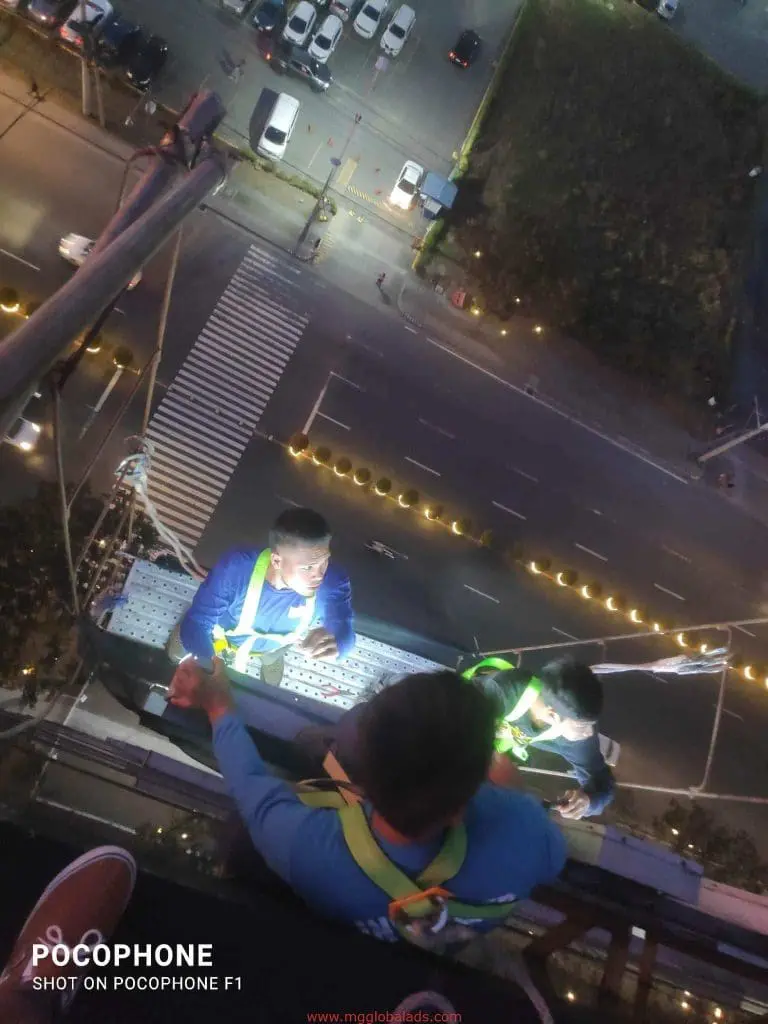 LED signage installation at night by three workers on a Makati building, with city lights and traffic, by M&G Global Ads.