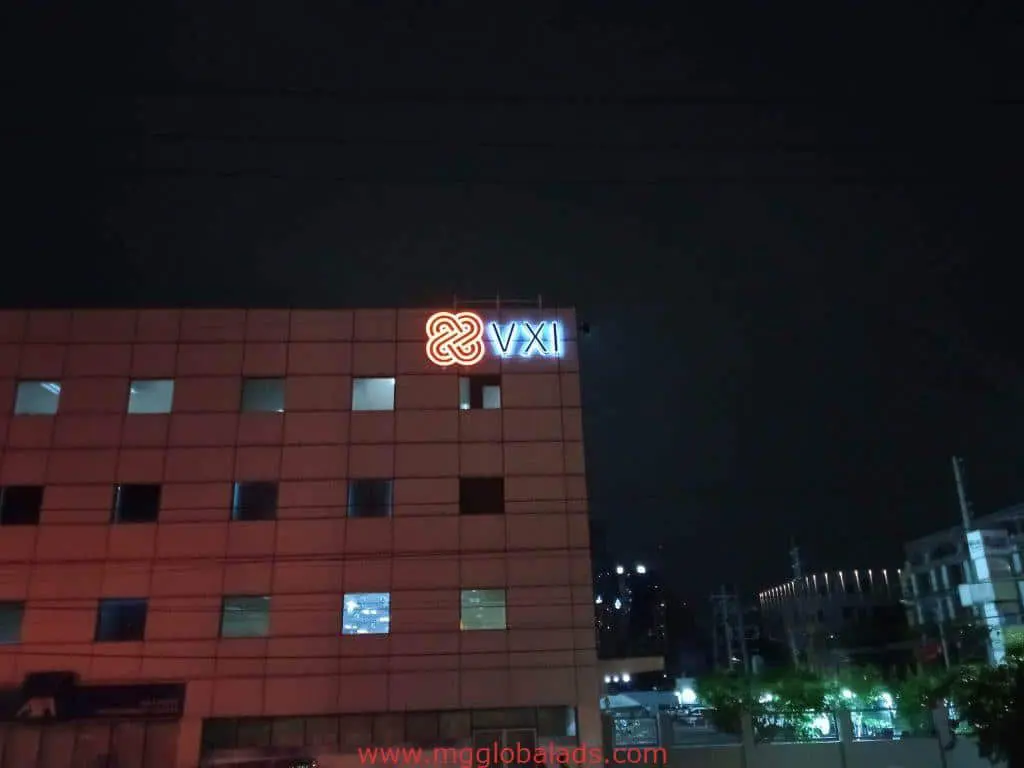 VXI LED outdoor signage on a high-rise in Mandaluyong at night with glowing windows and city lights, by M&G Global Ads.