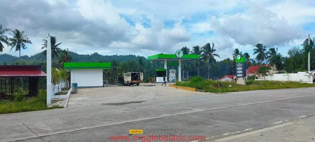 Gas station with green and white acrylic signage in Quezon City, road, palm trees, pickup, people by M&G Global Ads.