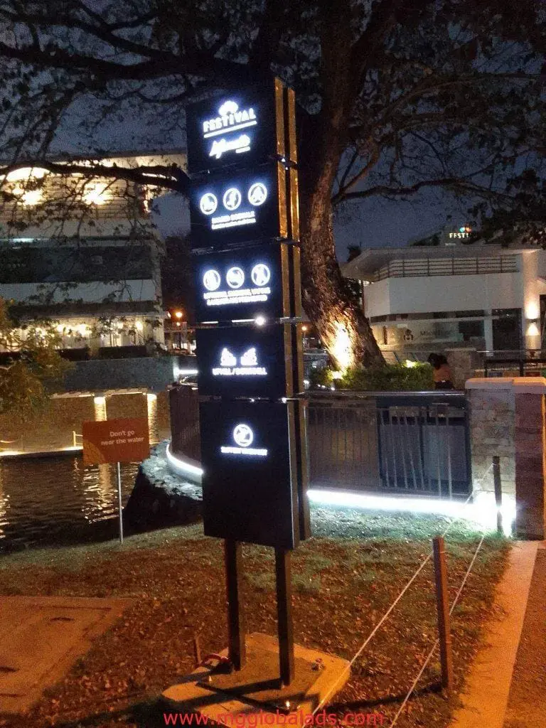 Festival Market wayfinding signage in Pasig at night near water, trees, and lit buildings by M&G Global Ads.