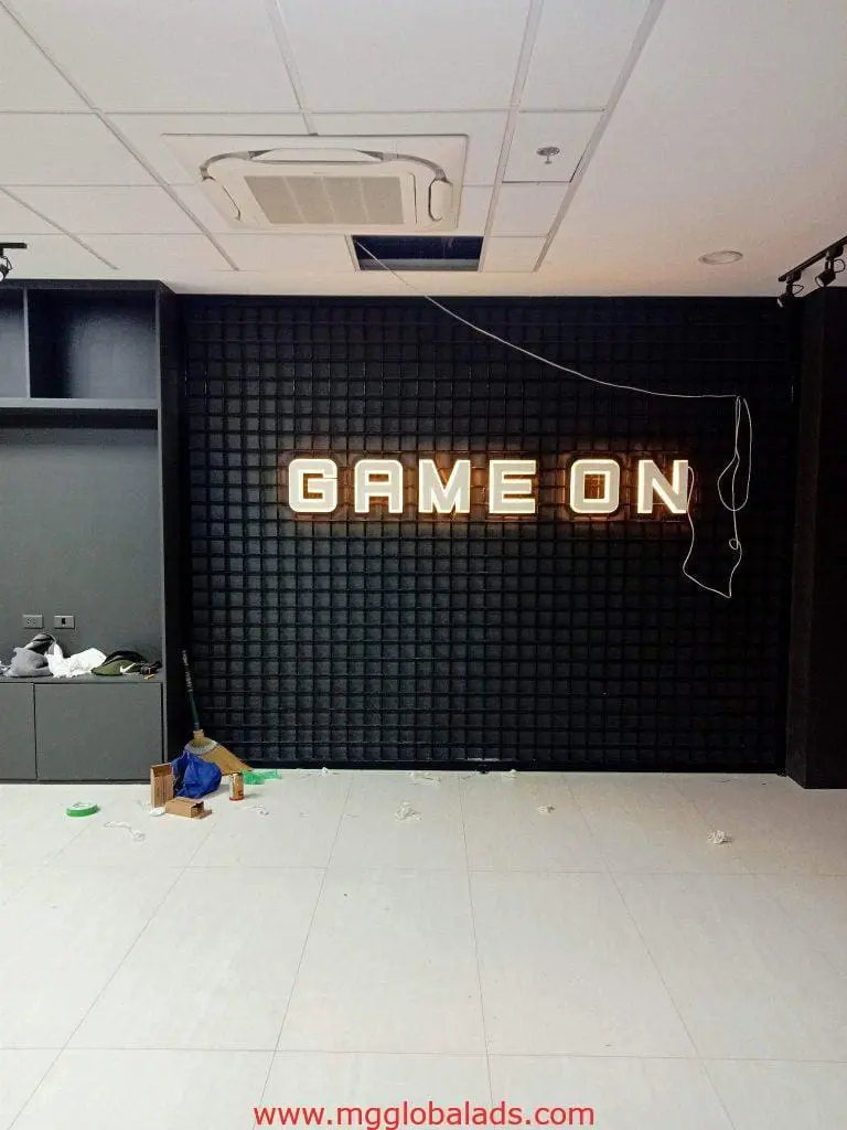 Illuminated LED GAME ON signage on black wall in modern Makati room with cleaning items, by M&G Global Ads.