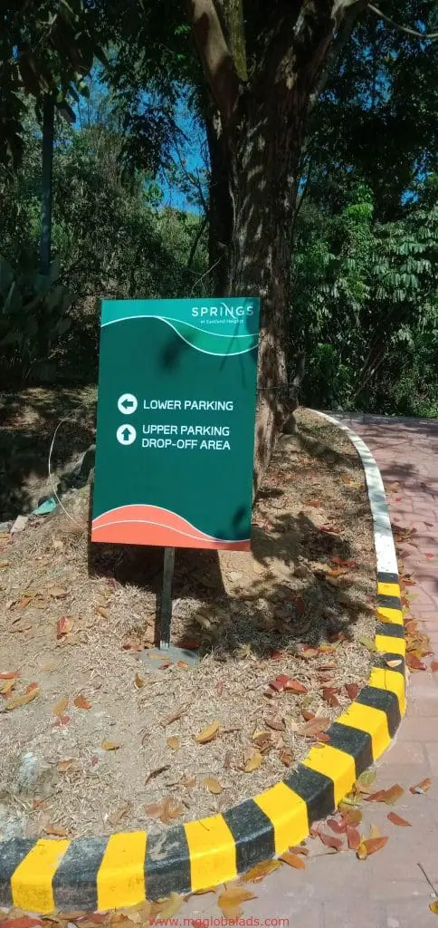 Wayfinding metallic sign for Springs parking directions beside curved path in Ortigas, yellow-black curb. By M&G Global Ads.