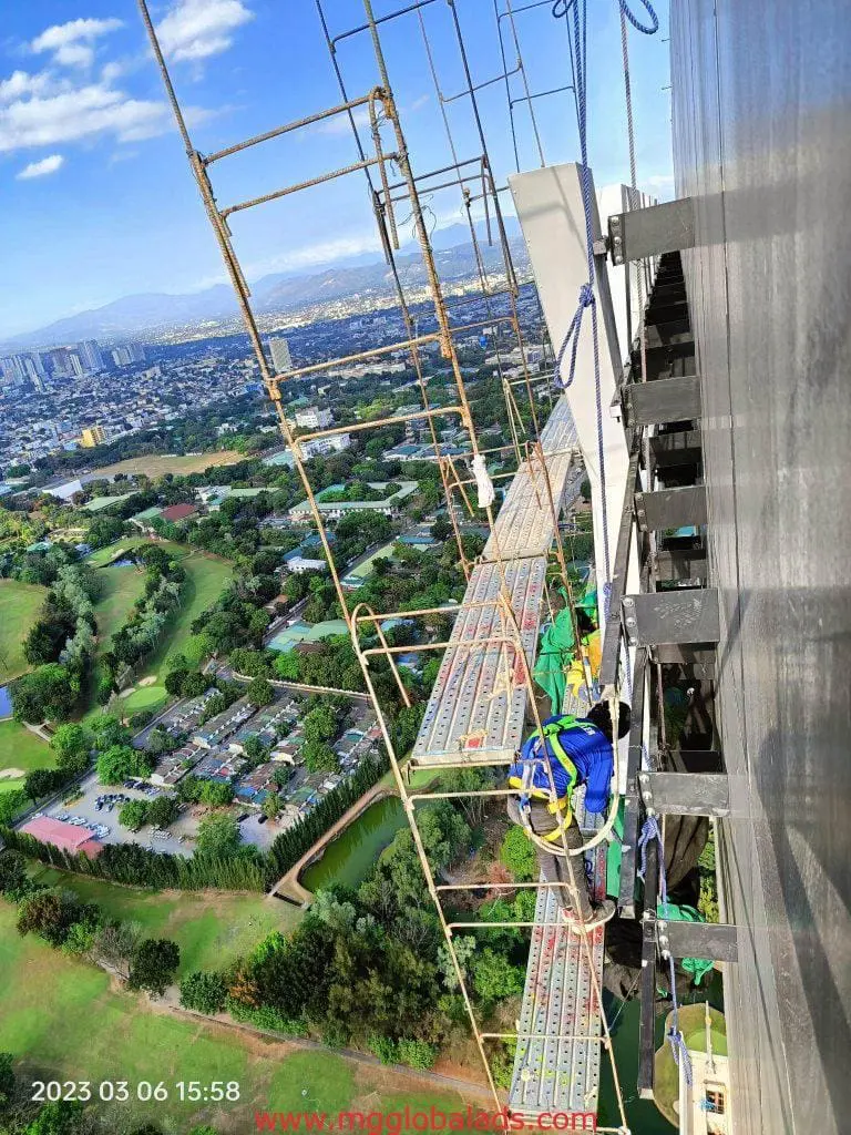 Metal sign installation on scaffolding in Quezon City skyline with safety harnesses, 2023-03-06 by M&G Global Ads.