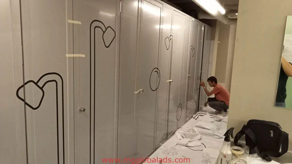 Restroom stall abstract line decal signage installation in a Makati office, tools and paper on floor, by M&G Global Ads.