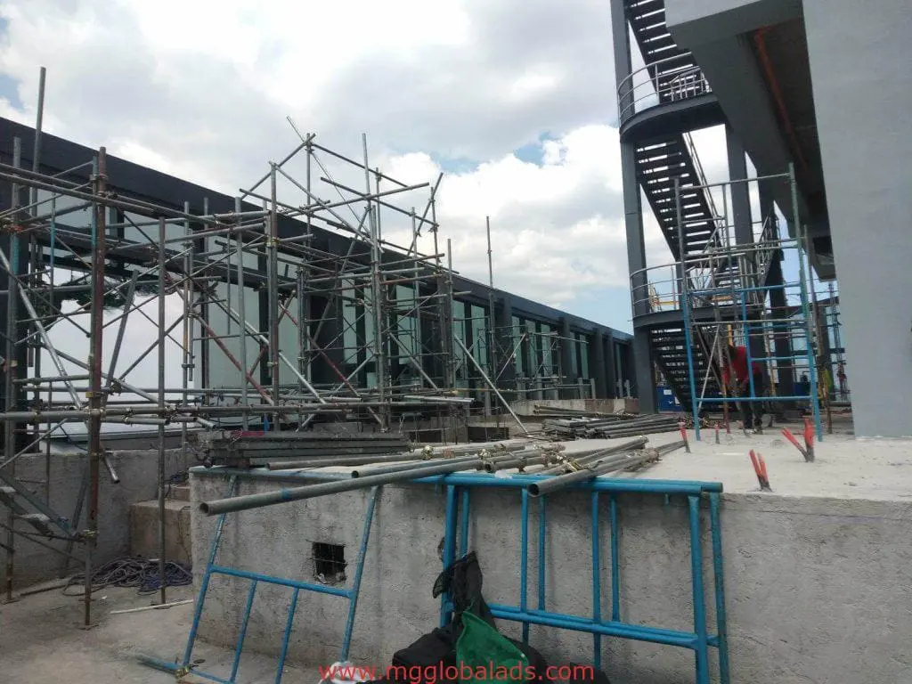 Construction site with metal scaffolding and billboard signage in Makati, spiral staircase visible, by M&G Global Ads.