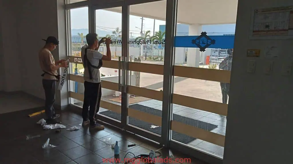 Office entrance door glass sticker installation with horizontal frosted strips and safety decals in Makati by M&G Global Ads.