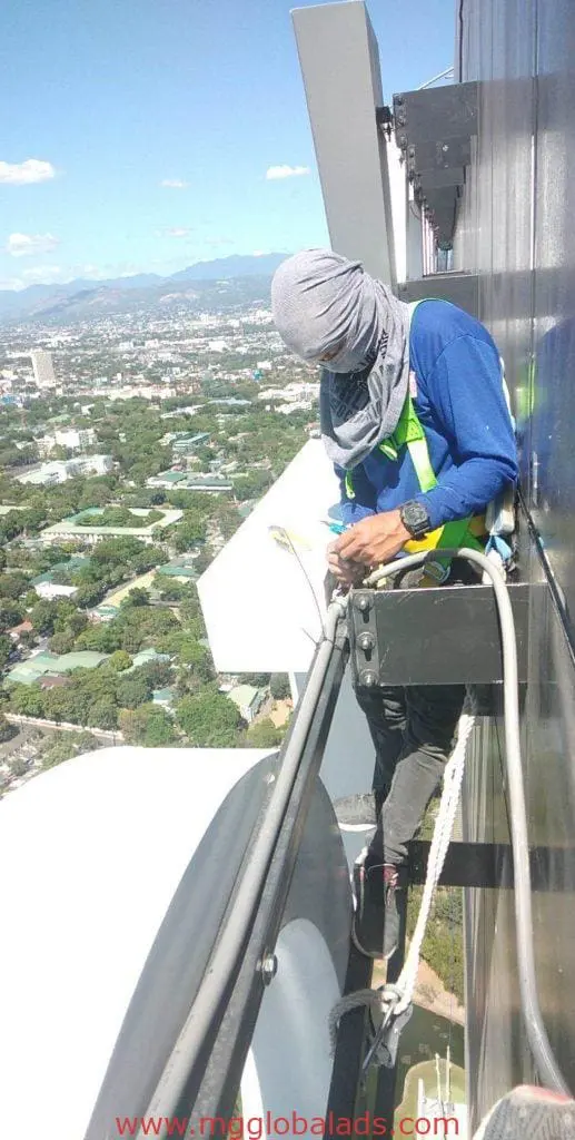 Worker harnessed for maintenance on metallic building signage in Makati, high above the cityscape, by M&G Global Ads.