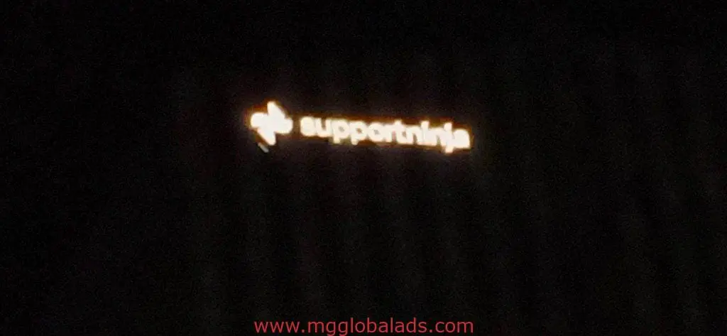 Blurry illuminated metallic sign for SupportNinja with white text, orange icon on dark background in Ortigas by M&G Global Ads.