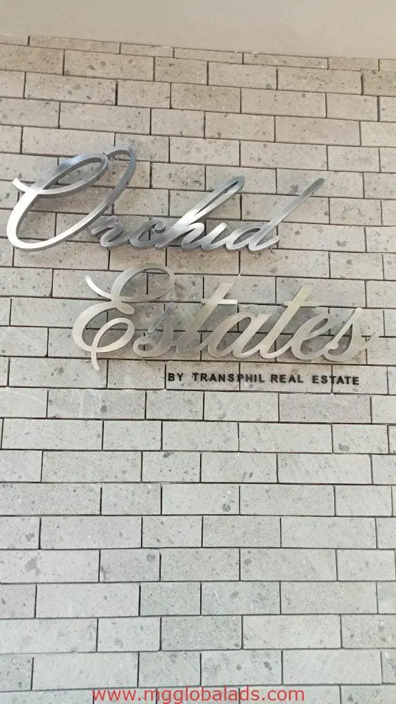 Stainless steel signage for Transhill Real Estate at Orchid Estates in Ortigas, mounted on white brick wall by M&G Global Ads.