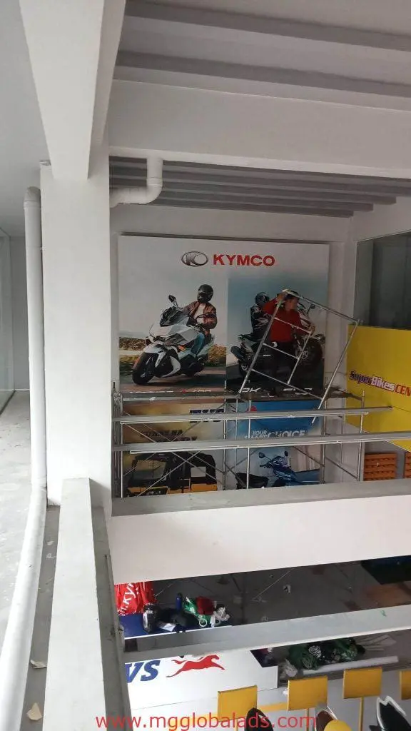 Kymco motorcycle indoor wall poster signage with riders, partly covered by metallic sign in Quezon City showroom by M&G Global Ads.