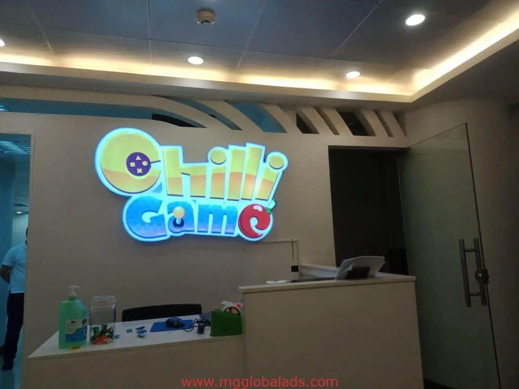 LED acrylic signage for Chilli Game in Makati reception area, behind a white desk with supplies. By M&G Global Ads.