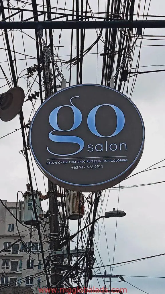 Round acrylic Go Salon signage with tagline and phone number on a busy Pasig street, by M&G Global Ads.