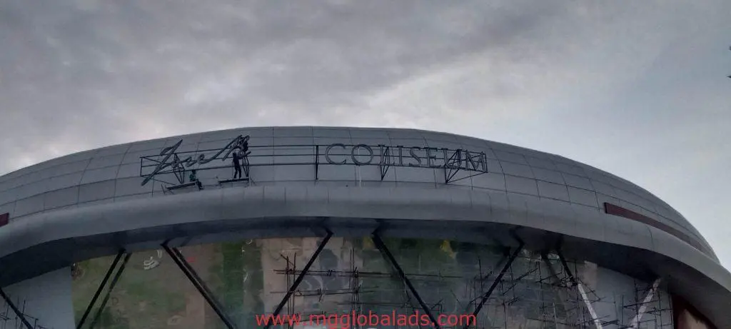 Acrylic signage for COLISEUM client on a large curved-roof building in Cubao with scaffolding and worker by M&G Global Ads.