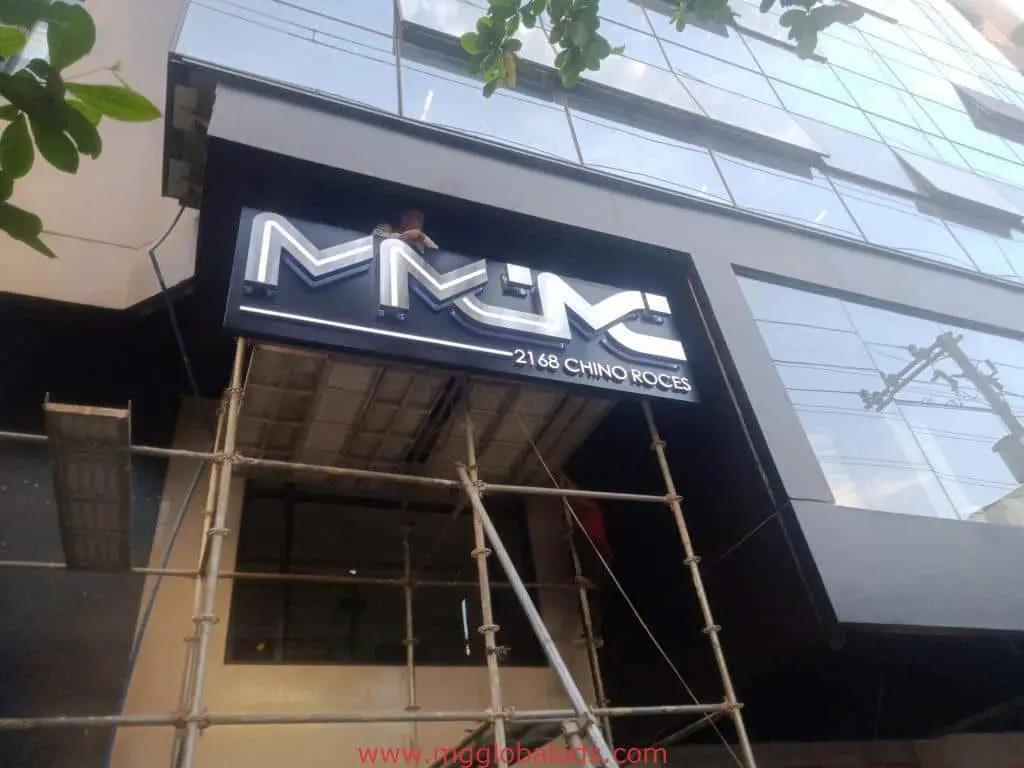 Illuminated metallic building signage for MNC 2168 CHINO ROCES, Makati location, by M&G Global Ads. Scaffolding and worker visible.