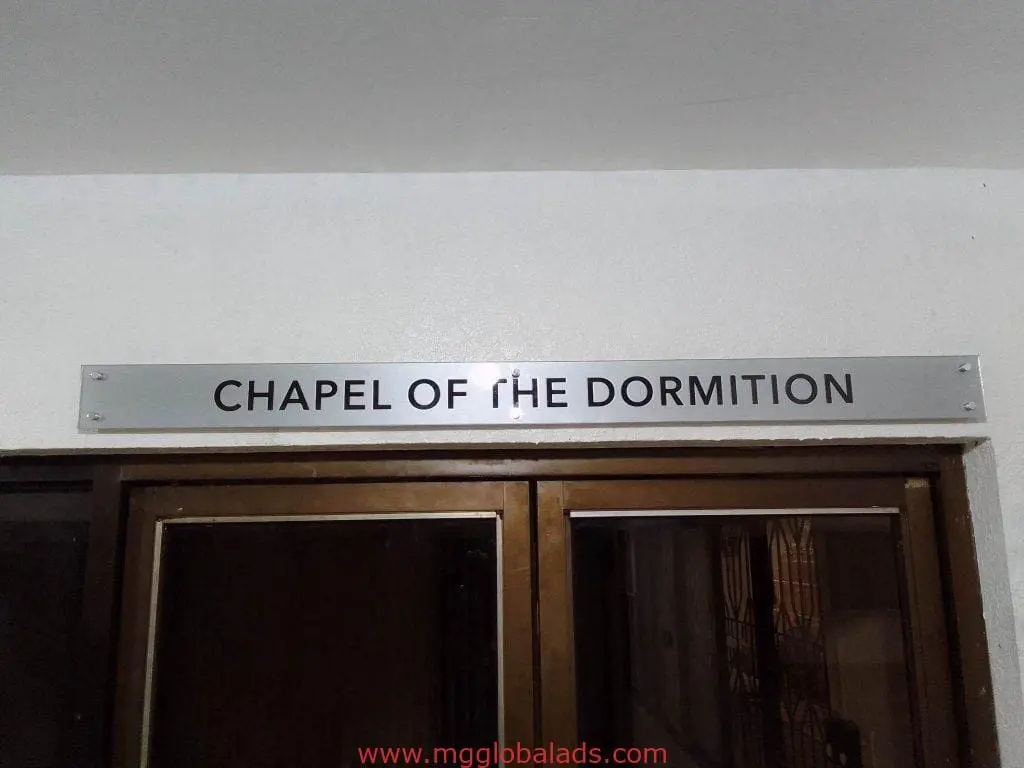Building signage for CHAPEL OF THE DORMITION in black letters on white wall, Quezon City location by M&G Global Ads.