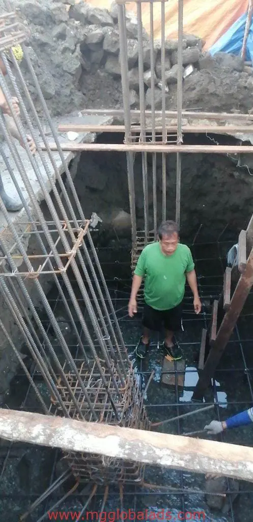 Billboard signage at a muddy construction site in Quezon City with worker and steel bars by M&G Global Ads.