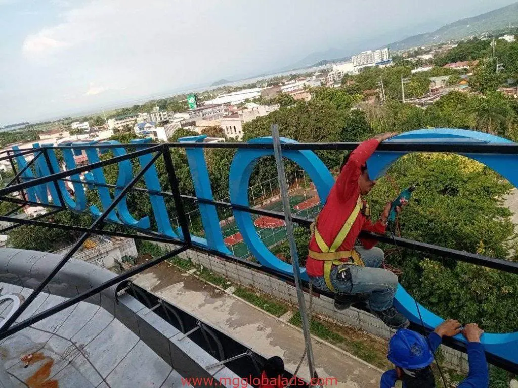 Acrylic channel letter signage installation on rooftop in Makati with cityscape backdrop by M&G Global Ads.