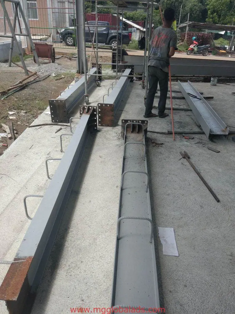 Construction worker with steel beams, rebar, and billboard signage in Makati construction site by M&G Global Ads.