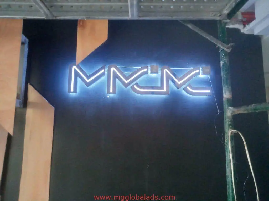 Neon indoor signage for MMMC with glowing white letters, construction scaffold, and wood panels in Ortigas by M&G Global Ads.