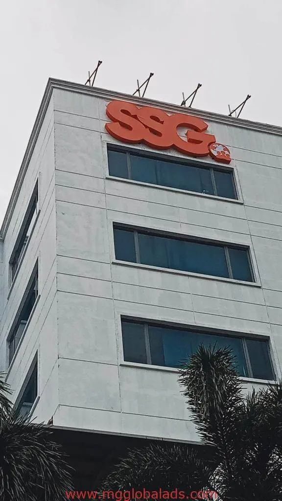 SSG metallic outdoor signage on white building with blue windows in Makati, palm trees in front, by M&G Global Ads.