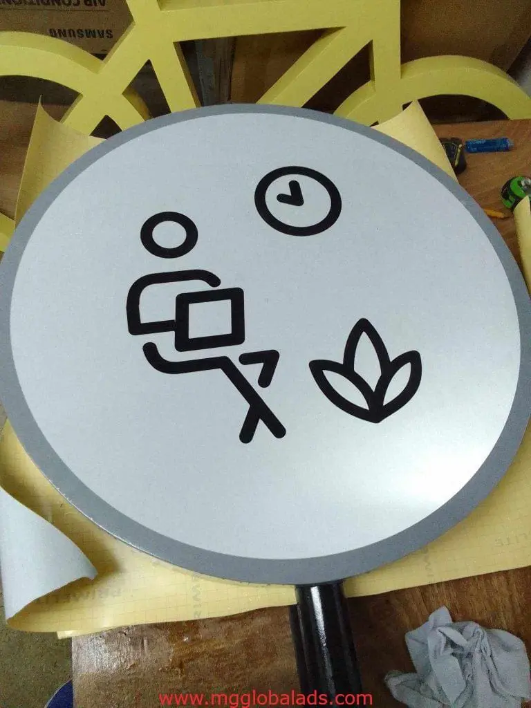Round metallic office signage in Makati shows stick figure with laptop, plant, and clock for break area by M&G Global Ads.