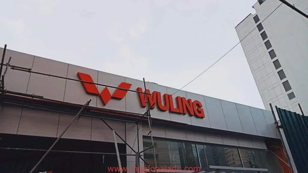 Wuling pylon signage and facade outdoor signs at dealership in Quezon City, with scaffolding and tall building, by M&G Global Ads.