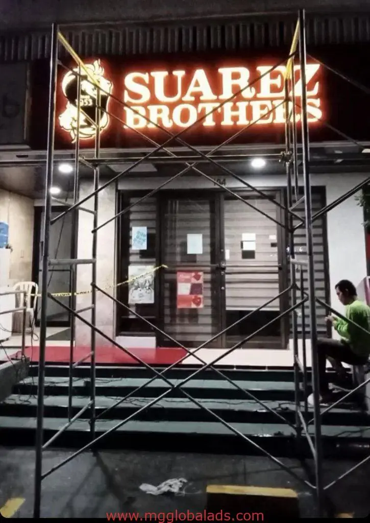 Suarez Brothers illuminated outdoor signage with scaffold at night, closed storefront in Ortigas by M&G Global Ads.