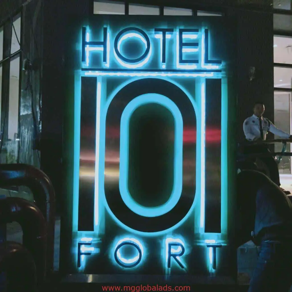 Neon metallic signage for HOTEL FORT in Makati, blue and pink glow at night with security guard, by M&G Global Ads.