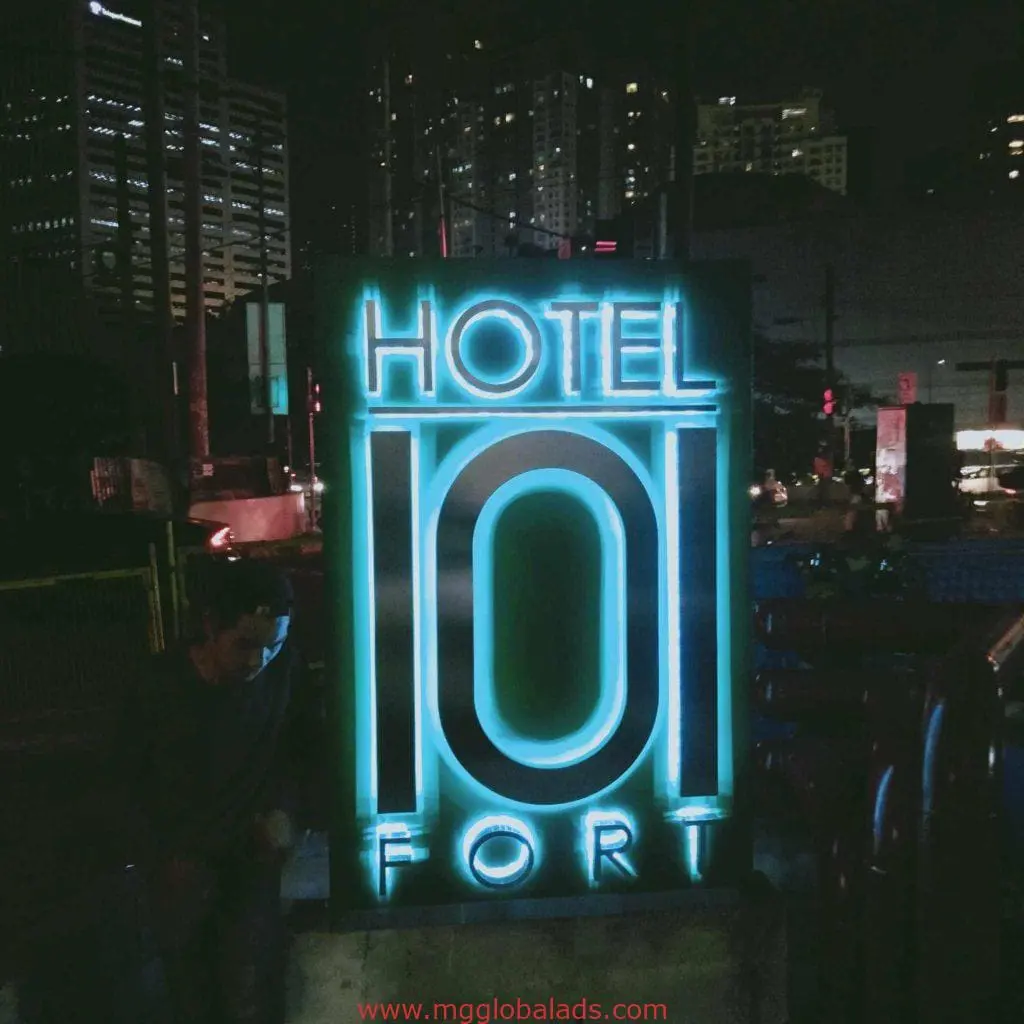 Neon outdoor hotel signage for HOTEL 101 FORT in BGC cityscape at night, person nearby. Signage by M&G Global Ads.