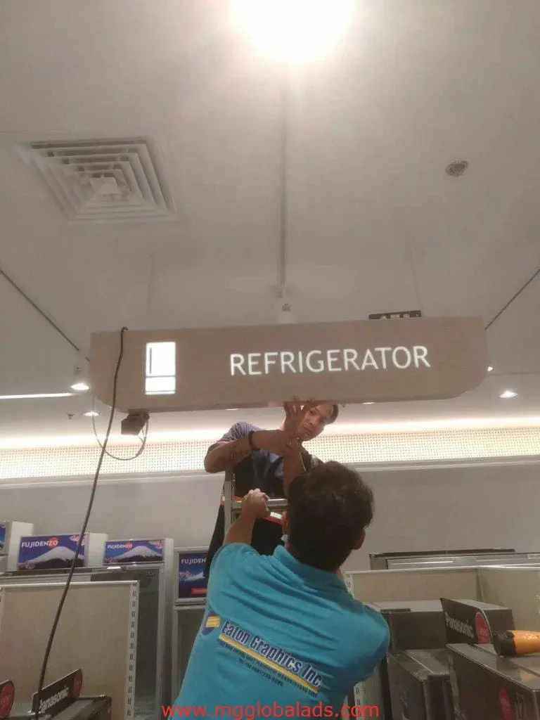 Indoor refrigerator signage installation in store, workers setting sign overhead in Makati by M&G Global Ads.