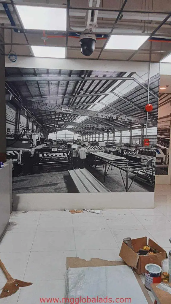 Factory-themed black-and-white photo mural and metallic signage in Makati, with paint cans on white floor by M&G Global Ads.