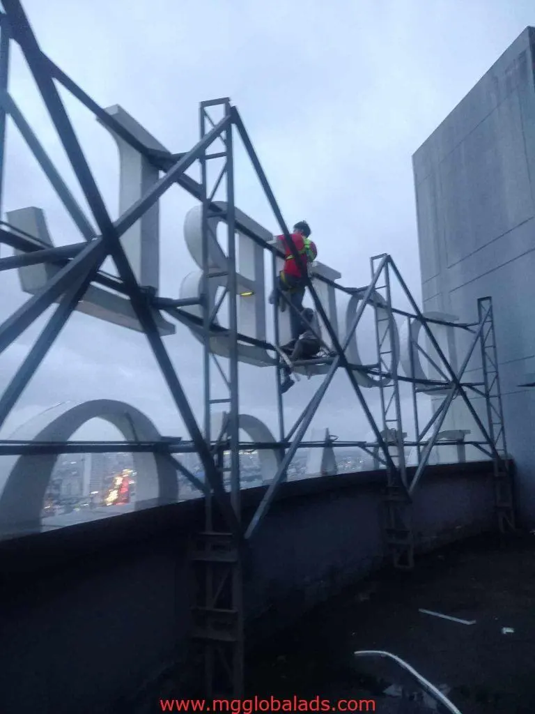 Outdoor LED signage installation showing worker in safety gear on city framework in Quezon City by M&G Global Ads.
