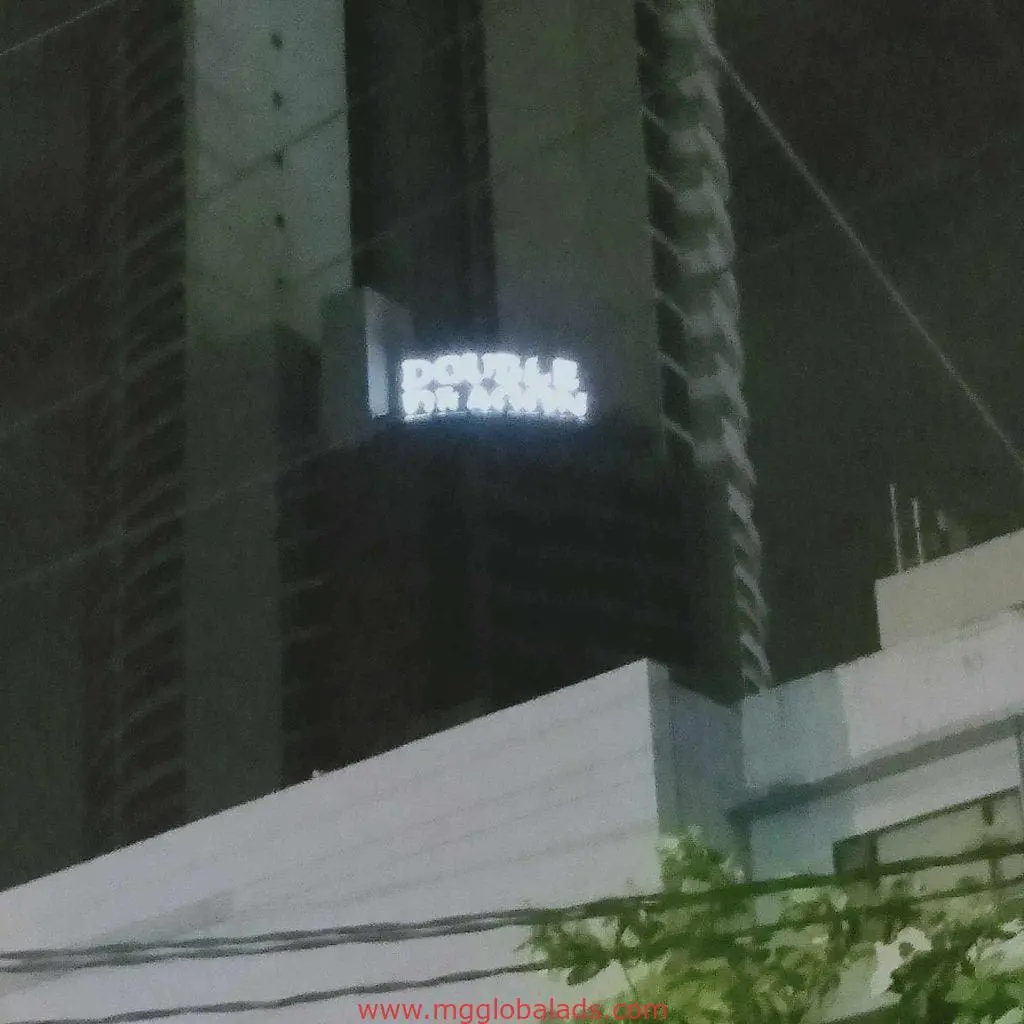 Illuminated DOUBLE outdoor building signage in Makati at night with power lines and tree branches, by M&G Global Ads.