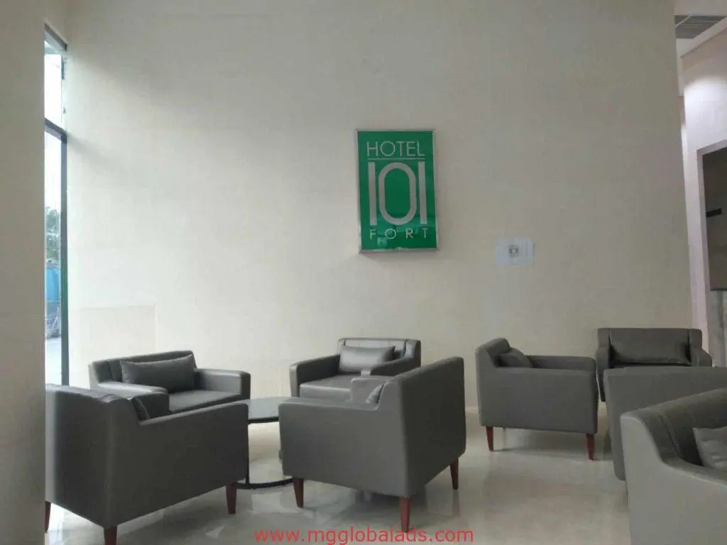 Acrylic HOTEL 101 FORT signage in a modern hotel lobby, gray armchairs, Makati location by M&G Global Ads.