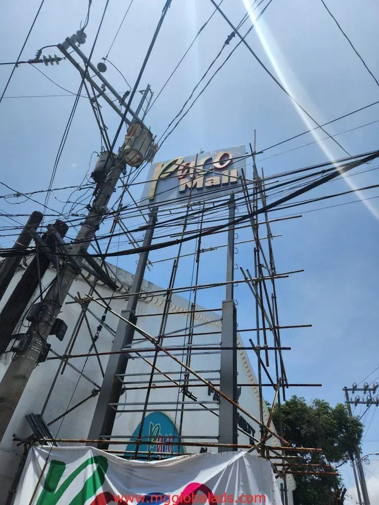 Outdoor metallic building signage installation atop scaffolding in Ortigas, with clear blue sky—by M&G Global Ads.